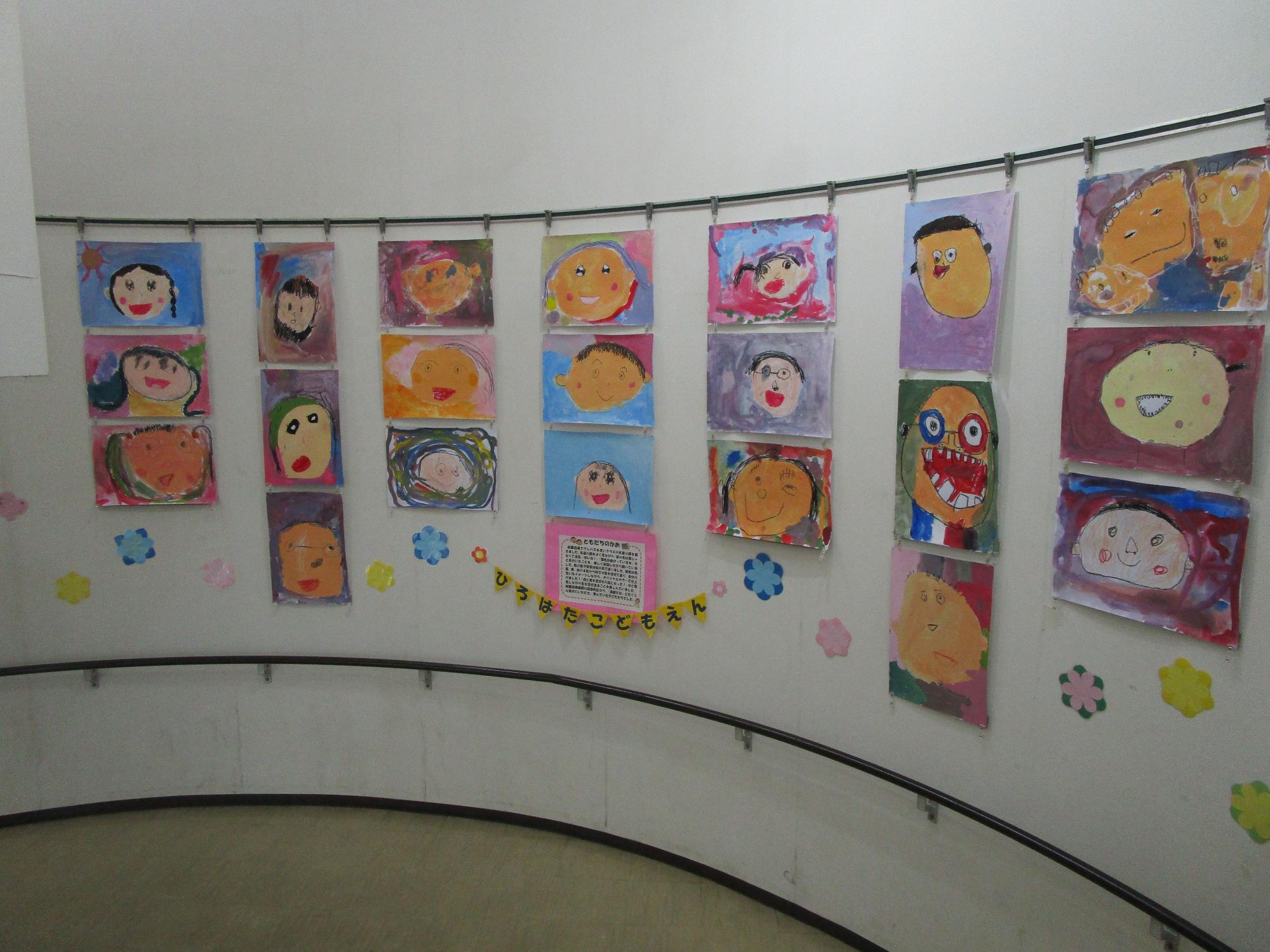 曲がった壁面に沿って、幼稚園児や小学生が描いたと思われるカラフルで表情豊かな人物画や自画像が展示されており、「ひろはたこどもえん」という文字が飾られた、明るく楽しい雰囲気の展示風景を捉えた写真
