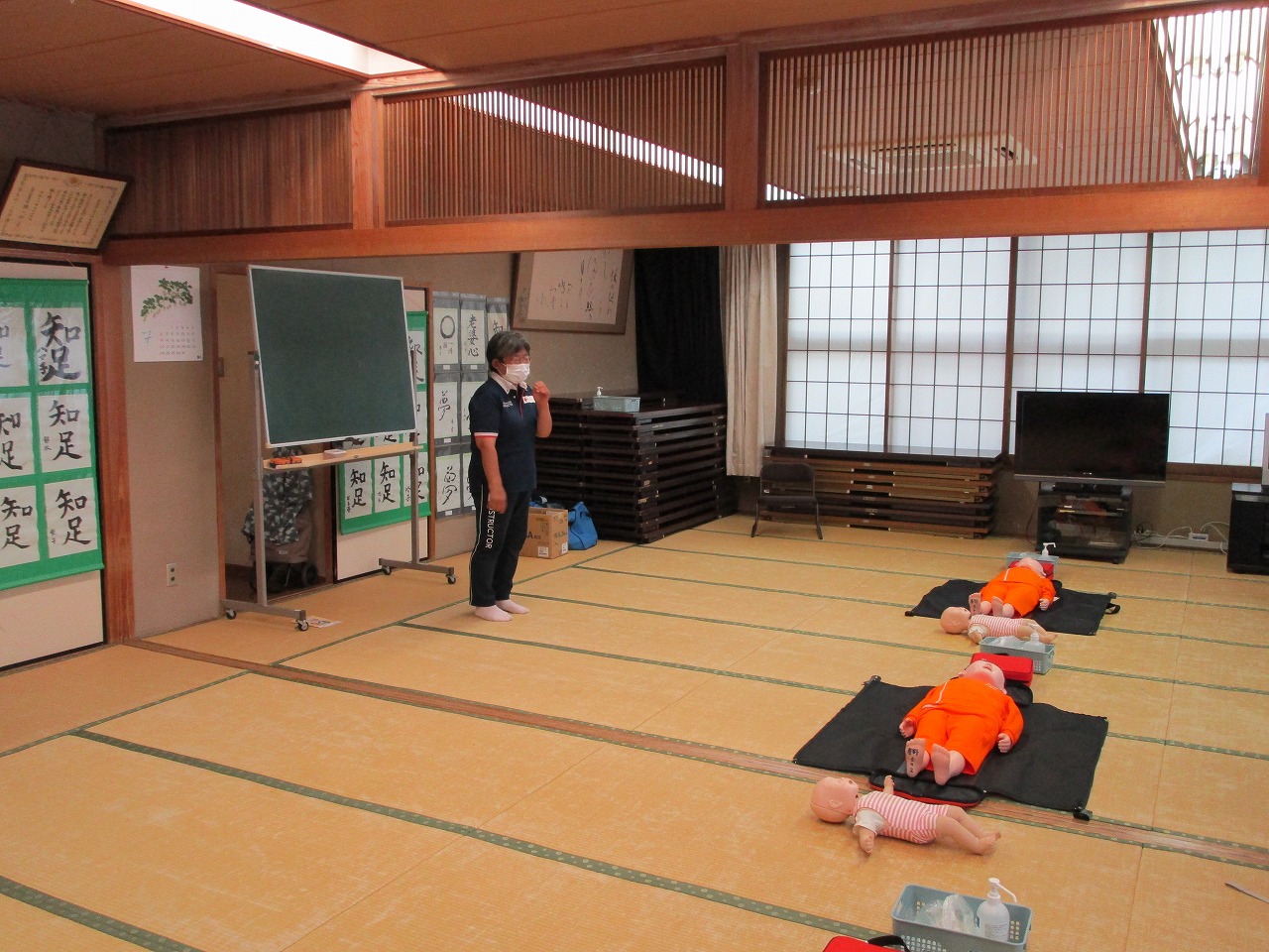 和室の畳の上で、講師の女性が立って説明をしており、心肺蘇生法の練習用マネキンが数体置かれた広い会場で行われている日赤幼児安全法講習の様子の写真