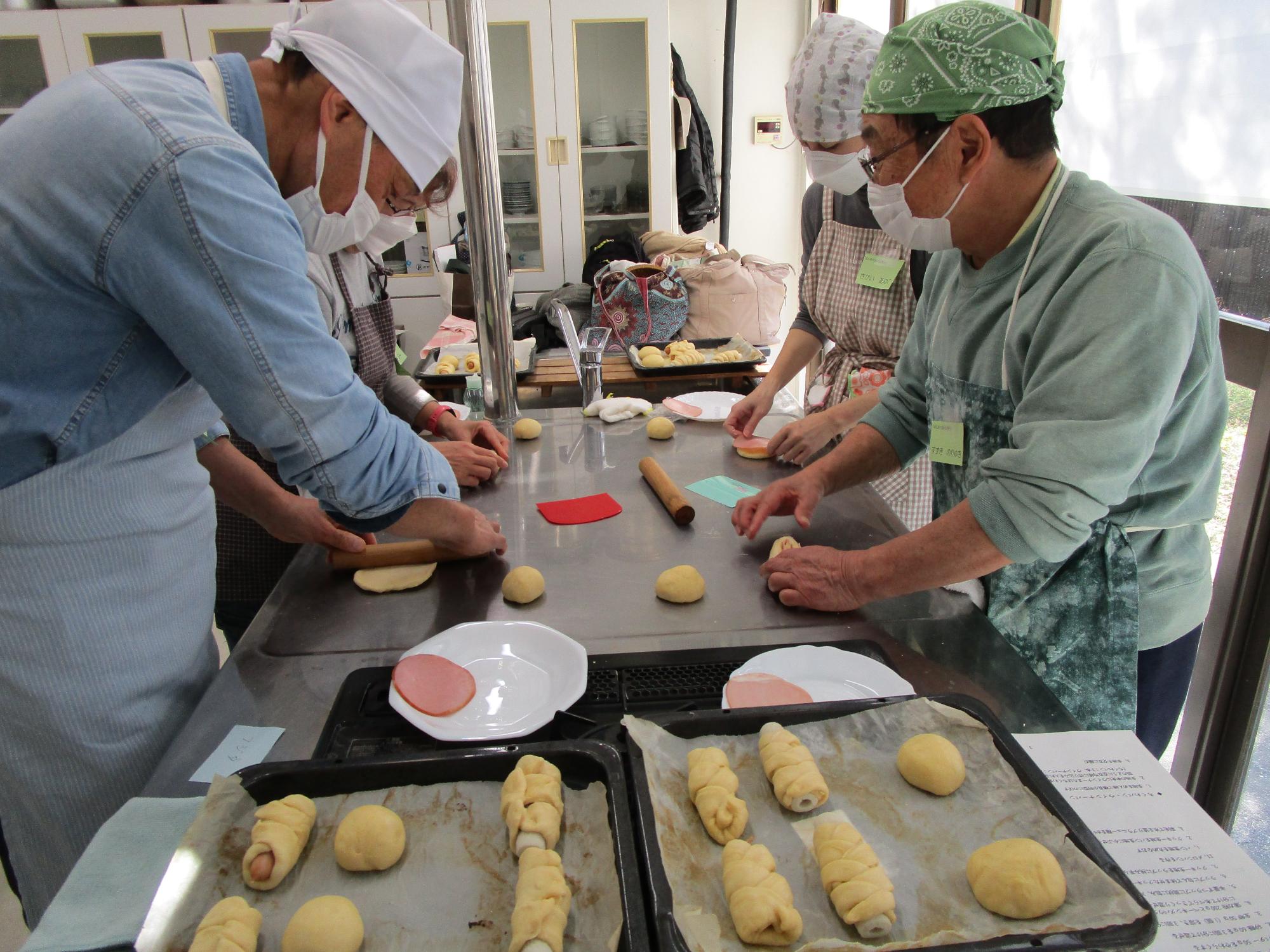 具が入れられたパン生地数個が天板に乗せられている。パンを作っている人が数人いる。