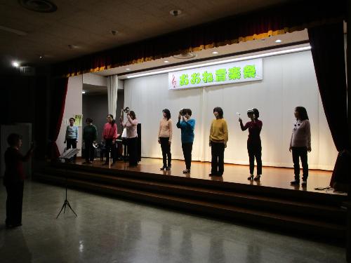 ステージ上で女性数名がコーラスを披露している、その中の数名は鍋をたたいてリズムを取っている。