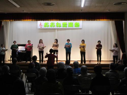 ステージ上で女性数名が譜面を見ながらコーラスを披露している