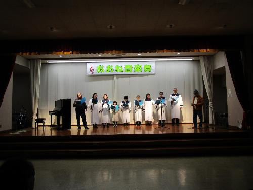 子どもを含む数名の白いガウンを着た聖歌隊がコーラスを披露している