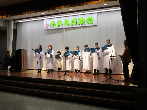 子どもを含む数名の白いガウンを着た聖歌隊がコーラスを披露している