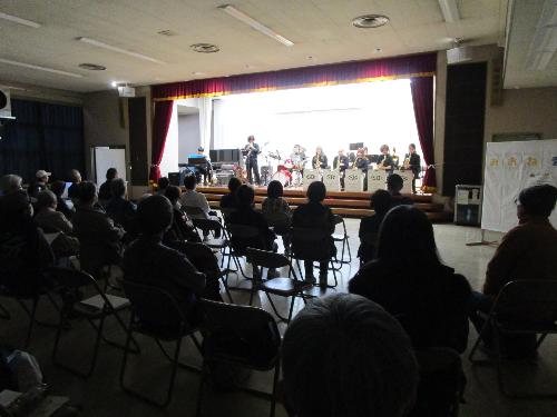 ステージ上で十数名がジャズ演奏を披露しているのを観客席から撮った写真