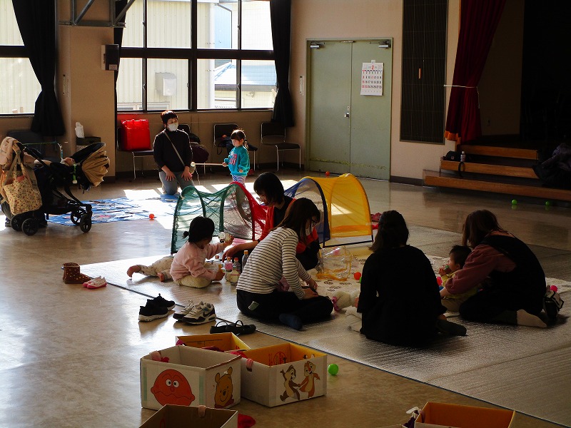 ホールの中で幼児数名が大人数名といろいろなおもちゃで遊んでいる