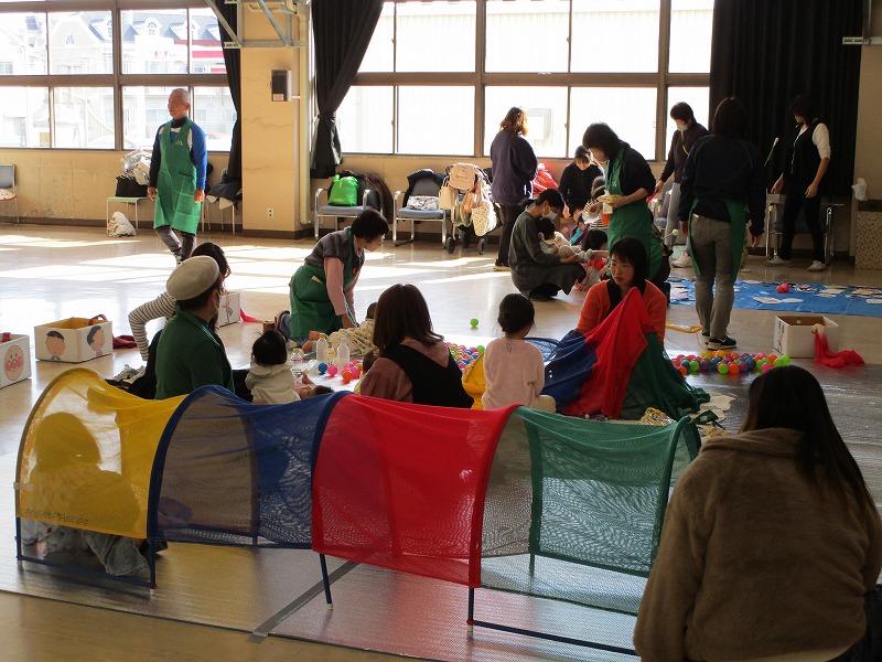 ホールの中で幼児数名が大人数名といろいろなおもちゃで遊んでいる