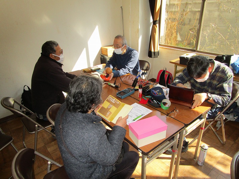 二人がおもちゃを修理していて、それを二人の大人が見ている。