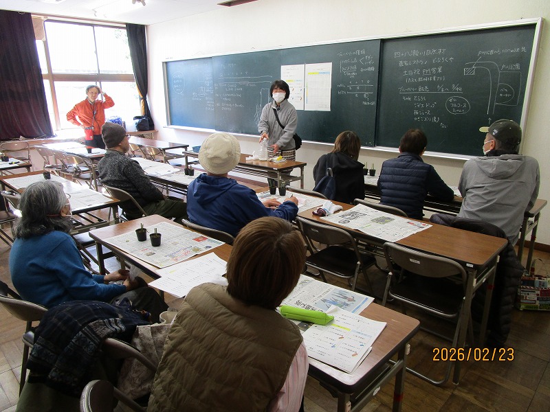 講師がシイタケの植菌について説明しているのを大人10人くらいが聴講している。