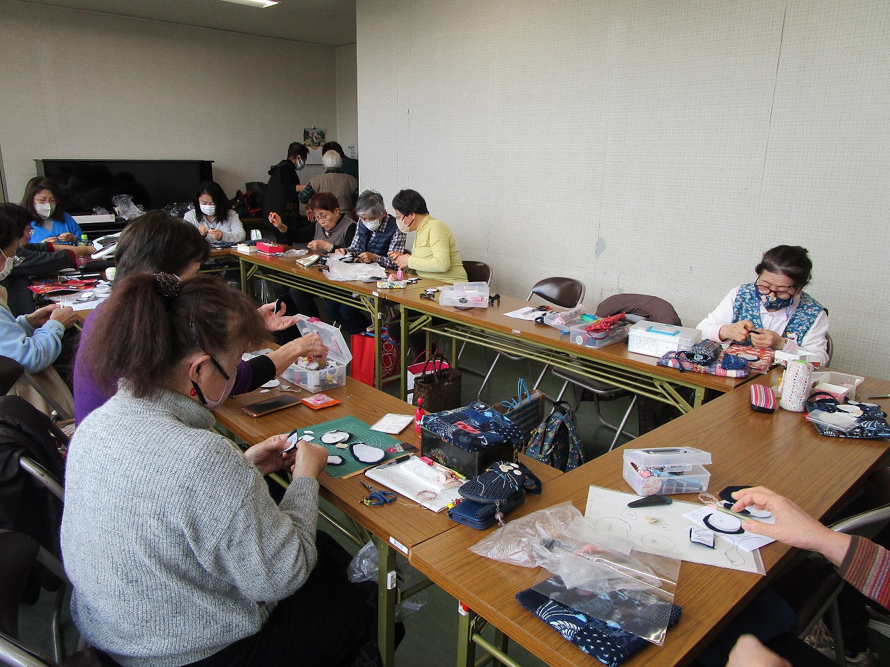 女性十数人が机に着席して縫い物をしている。