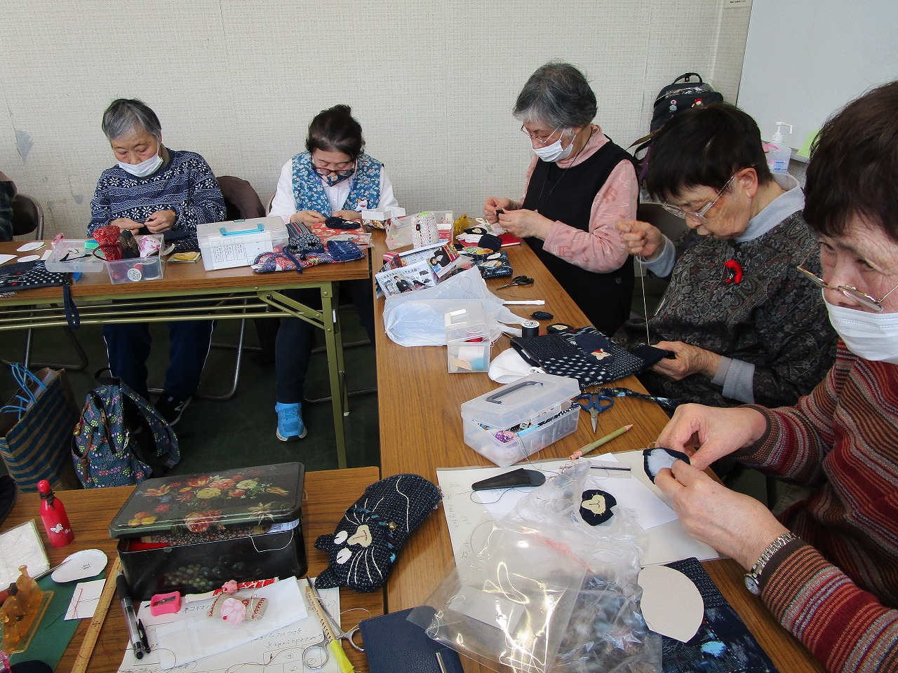 女性数人が机に着席し縫い物をしている。