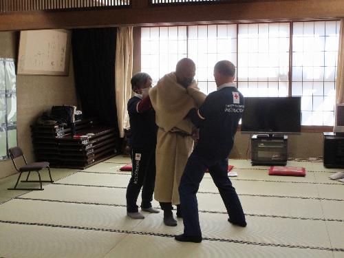 大人の男性を防寒のために二人で毛布で包んでいる様子