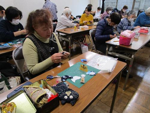 十数人の女性が机の上で縫物をしている様子