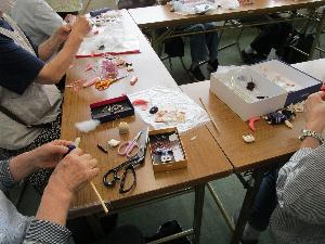 テーブルの上に針仕事の道具が置かれて、数人の人が針仕事をしている様子