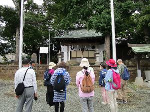 神社の境内で神社について講師が数人の大人に説明をしている様子