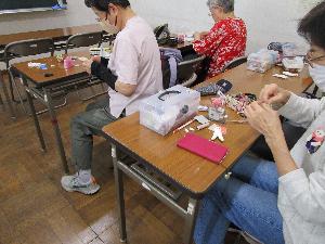 数人の大人が椅子に座ってテーブル上で針仕事をしている様子