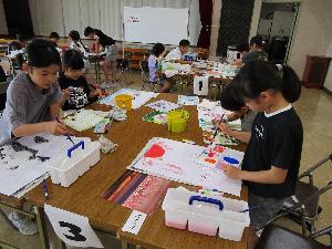 複数のテーブルそれぞれで、小学生数人が水彩画を描いている様子