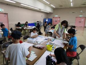 複数のテーブルそれぞれで、小学生数人が水彩画を描いている様子
