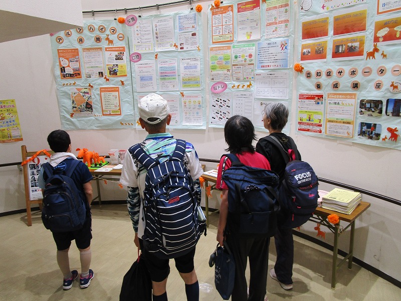 壁に展示されている資料を数人の大人が見ている