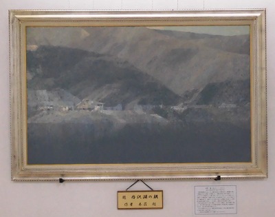 額縁に収められた、彩度を抑えた落ち着いたトーンで描かれた丹沢湖の絵とその下のネームプレートにタイトルと作者が書かれた写真