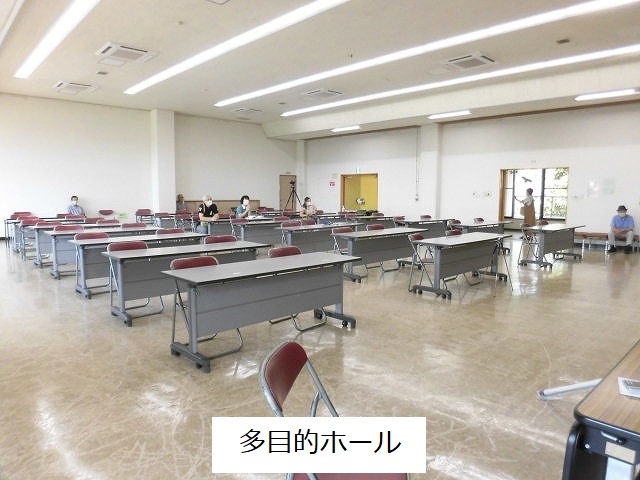 明るく広々としたキャスター付きの机と折りたたみ椅子が整然と並べられている多目的ホールの写真