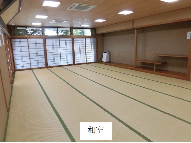 広々とした和室で、部屋の奥には障子戸が並び、畳が敷き詰められ、部屋の右側には木製の棚がある和室の写真