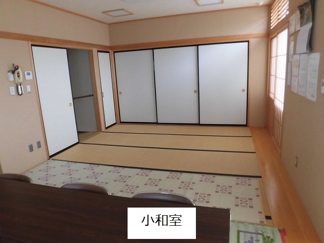 手前の一部にはクッションフロアが敷かれ、濃い木目調のテーブルと椅子が置かれ、奥には畳のスペースが広がり部屋の壁一面には白い襖が並んでいる小和室の写真