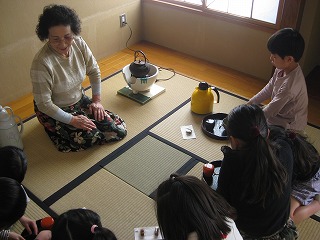 和室で数人の子どもたちが畳に座り、女性から指導を受けながら茶碗にお茶を点てている茶道教室の様子の写真