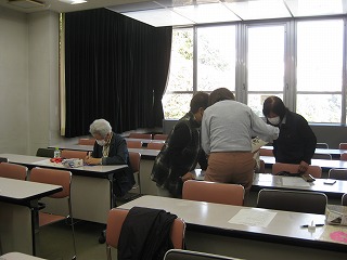 椅子に座った数名の生徒が机を使い、一部の生徒は立ち上がって資料を覗き込むなど、各自が熱心に作業に取り組んでいる様子を撮影した写真