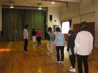 広々とした木製の床の部屋で、数名の女性がラダーを使い、先頭の講師に続いて歩行訓練を行っている様子を捉えた写真