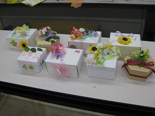色とりどりの造花やリボンで装飾された大小様々な白い箱が机の上に並べられている様子を映した写真