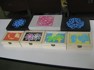 白木と黒い箱にカラフルな切り絵が飾られた複数の作品がテーブルに並べられており、蝶や花、紅葉といった様々な模様が精巧に表現されている様子の写真