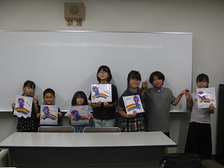 男女7人の子供たちがホワイトボードの前でそれぞれの作品を手に、楽しそうにカメラに向かってポーズを決めている様子の写真