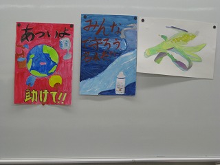 「あついよ助けて！！」と書かれた地球のイラストや、「みんなで守ろう未来」と書かれた水資源をテーマにしたイラストなど、複数の環境問題に関する作品が展示されている様子の写真