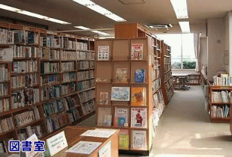 明るい照明の下、壁面や中央に複数の書架が並び、右奥の窓際には閲覧用の机と椅子が配置されている、「図書室」と記された静かで整然とした図書館内の空間を写した写真