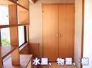木目調のクローゼットのような両開きの収納扉と、左奥には木製の棚が一部見える部屋の一角を捉えた写真で、下部には「水屋、物置、棚」の文字が重ねられている屋内写真