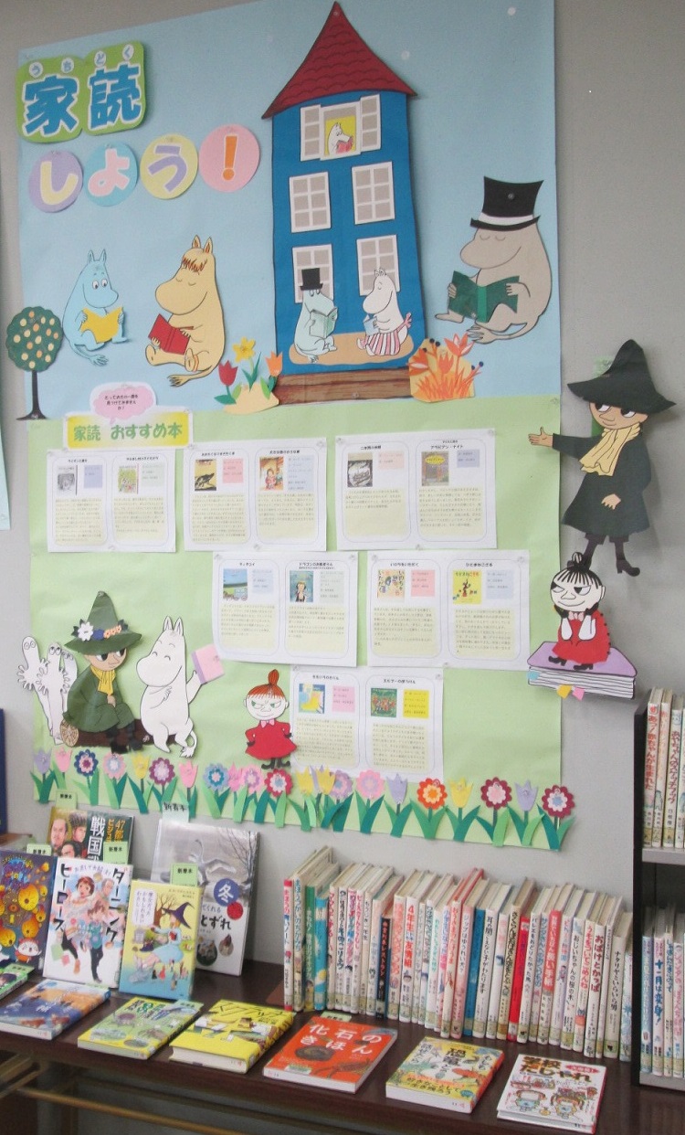 ボール紙の台紙に黒い紙が貼られ、白抜きで「図書室」と書かれたプレートの周りを、赤いワンピースと青いサロペットを着た二匹の黄緑色のクマの切り紙や、テントウムシと葉っぱのモチーフで装飾した、愛らしい掲示物の写真