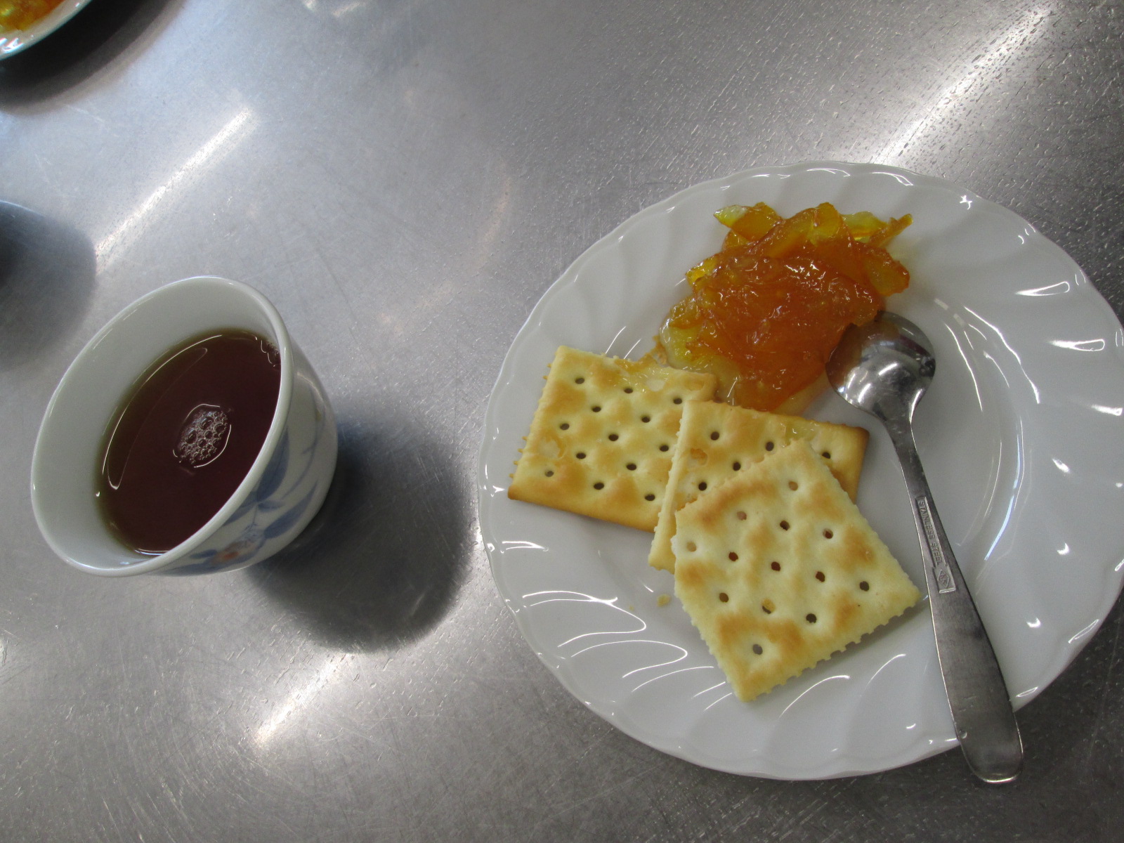 クラッカーとスプーン一杯のマーマレード、カップのお茶が並んだ写真