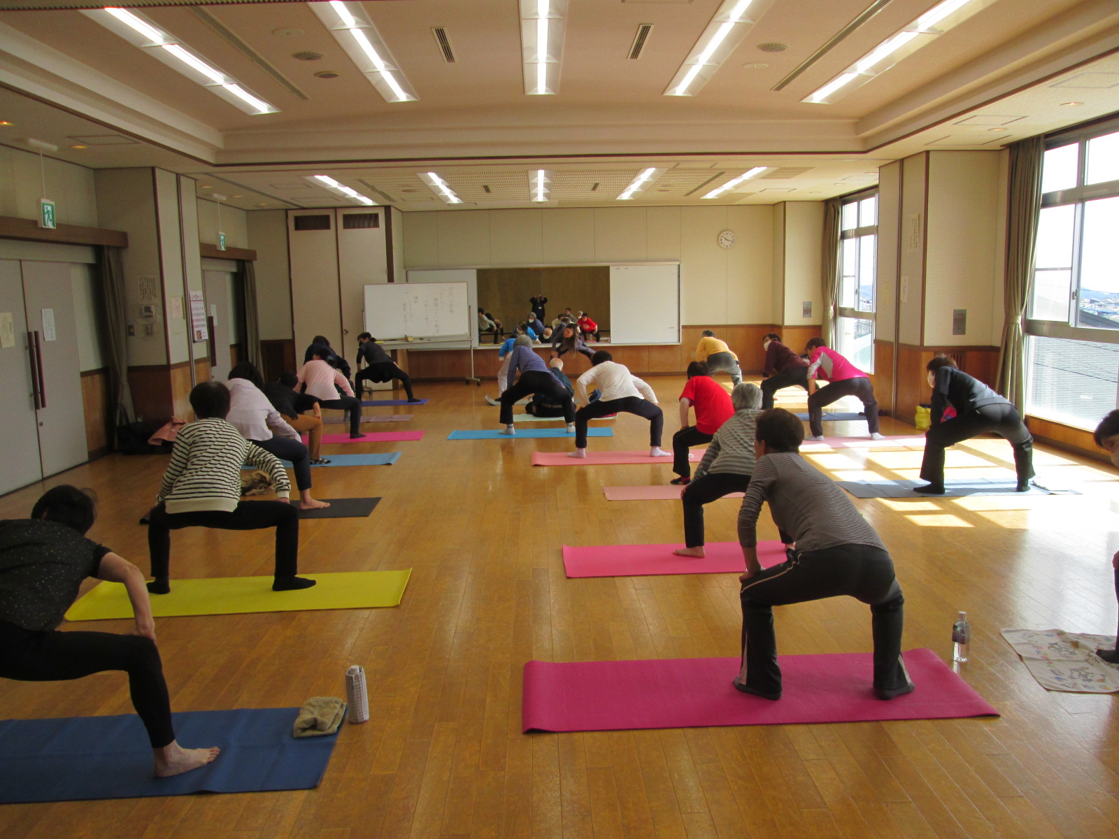 ヨガ教室で、参加者が足を肩幅に開いてスクワットの姿勢をとっている様子を写した写真