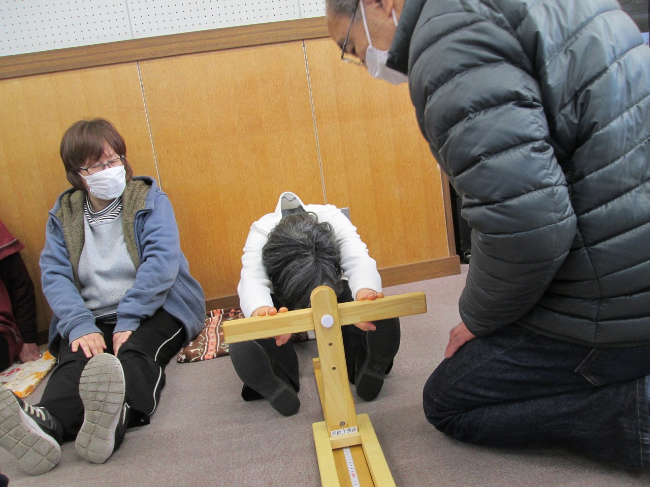前屈測定器の前に座り前屈をしている女性と、測定結果を確認している男性の写真