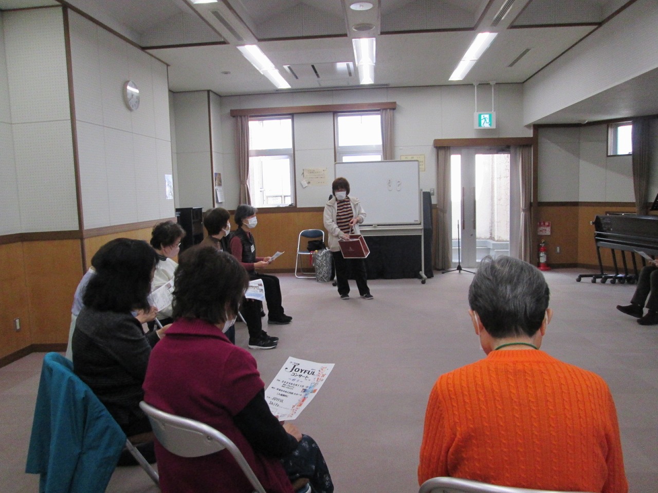 ホワイトボードの前に立って話している女性と、周りの席に座った参加者たちの様子を写した写真