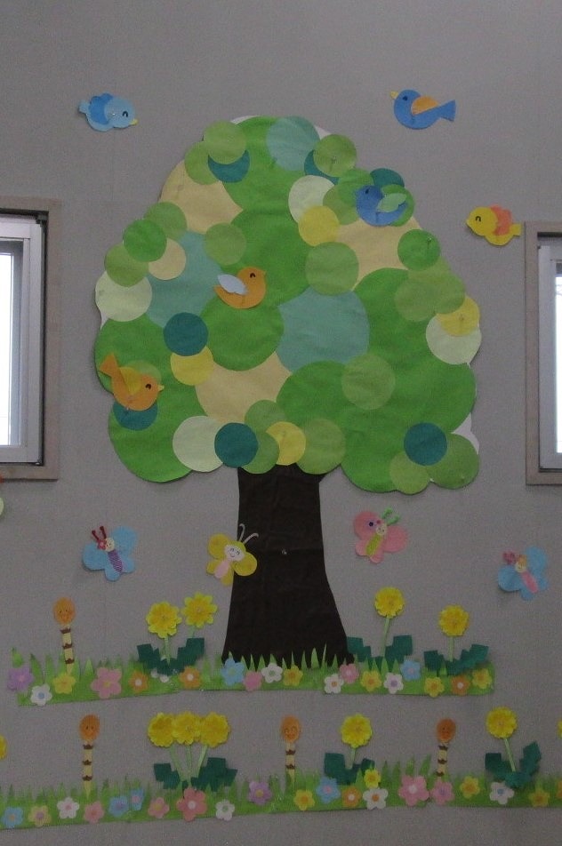 水色の台紙の上に、濃いピンク、薄いピンク、紫色の切り紙で作られたコスモスのような花々が一面に咲き乱れる様子が表現され、白い雲と赤と白の切り紙のトンボが飛んでいる、賑やかな壁面装飾の写真