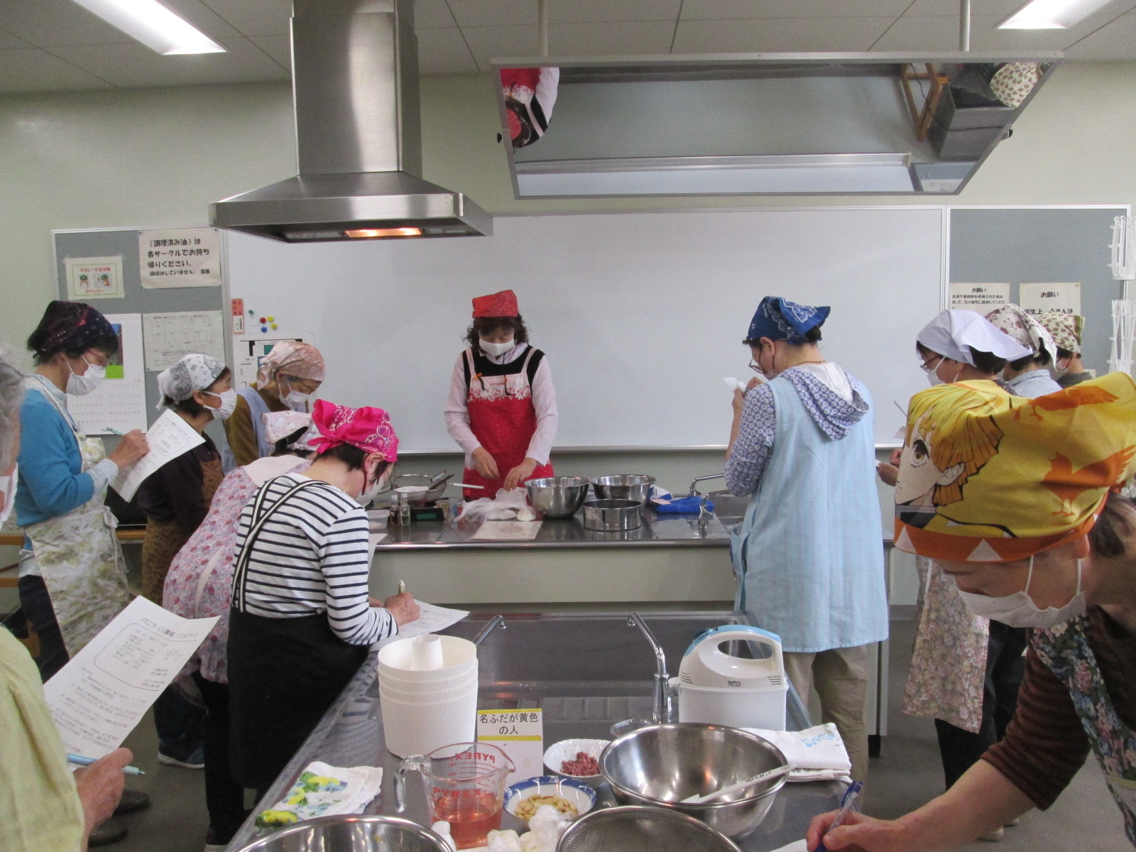 料理教室で、参加者が講師の説明を聞きながら調理台の前で食材を扱っている様子を写した写真