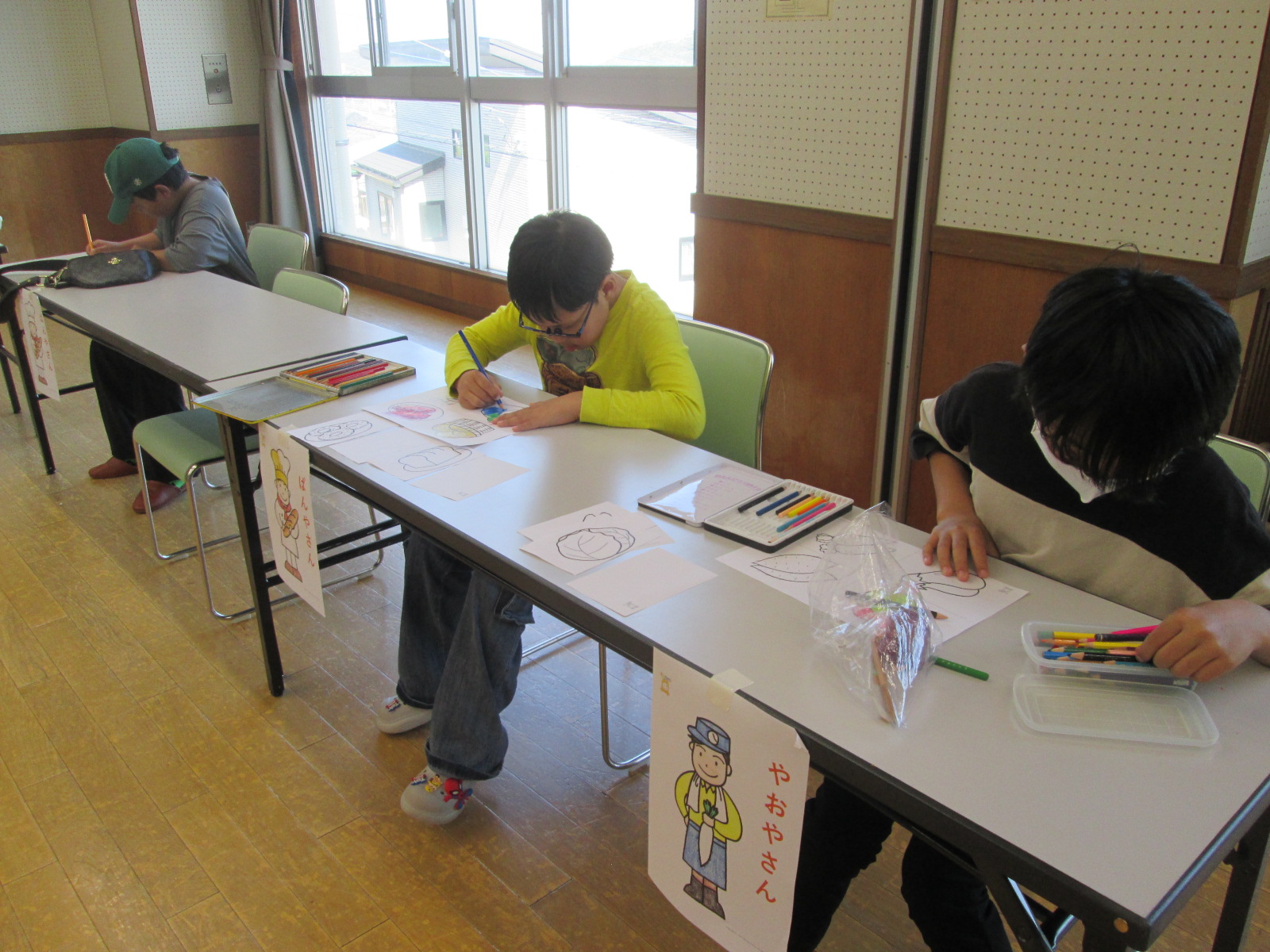 子供たちが机に向かって色鉛筆などを使い、集中して絵を描いている様子を写した写