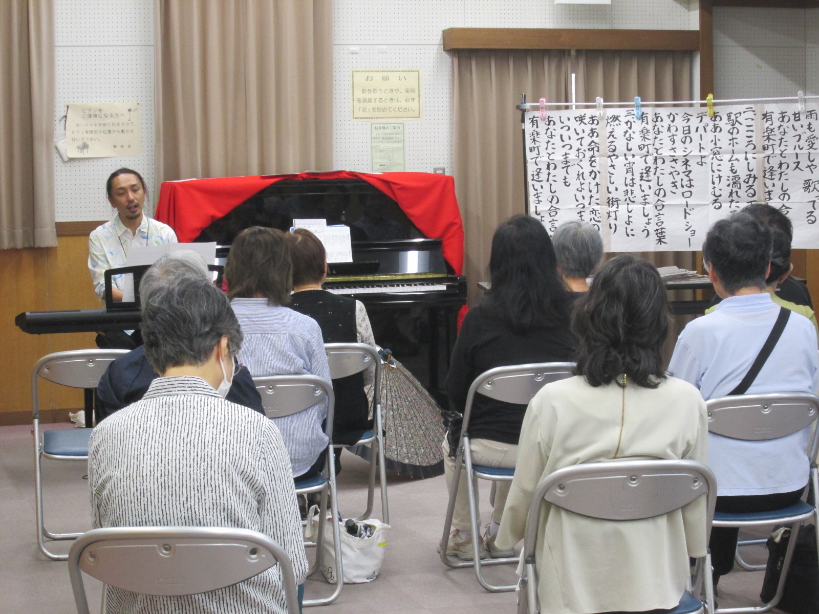 室内で行われている音楽教室で、電子ピアノの前に座った三野先生を参加者席の後ろから撮影した写真