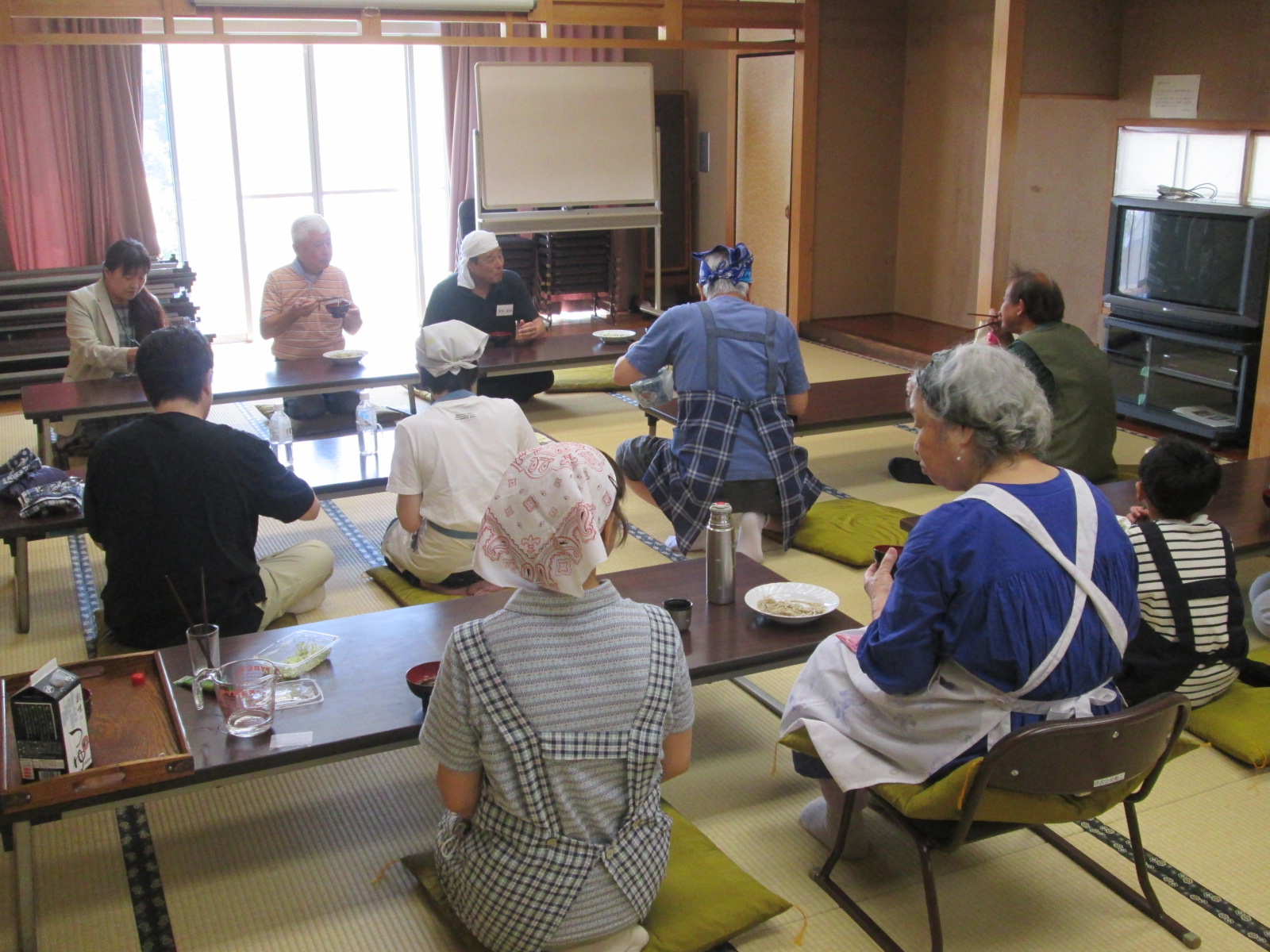 畳のある和室で、複数の人が食事をしながら楽しそうに談笑している様子を写した写真
