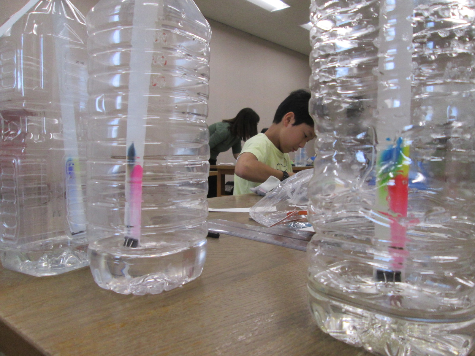 空のペットボトルに水を入れ、ストローとマーカーを使って水圧で浮き沈みするおもちゃを子供たちが制作している作業風景の写真