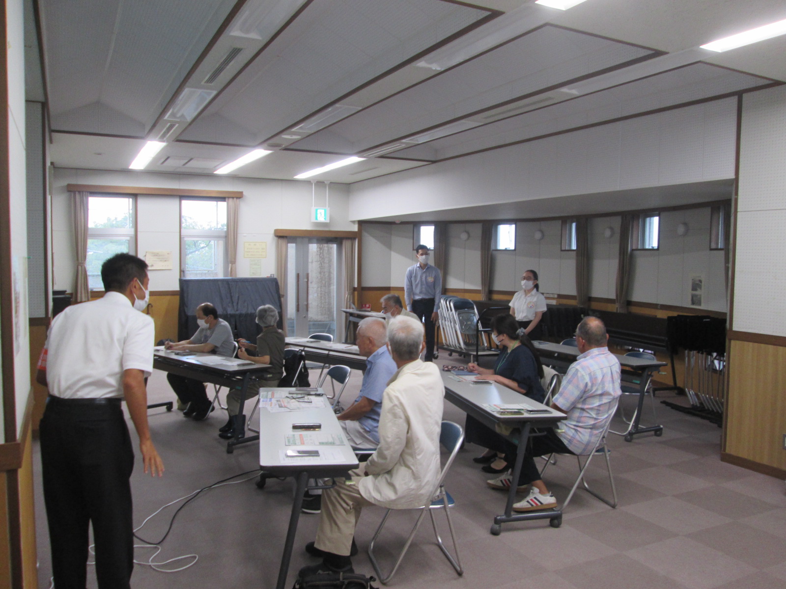 中高年を対象としたスマートフォン教室で、マスクを着用した講師が受講者一人ひとりの机を回りながら個別に操作方法を指導している写真