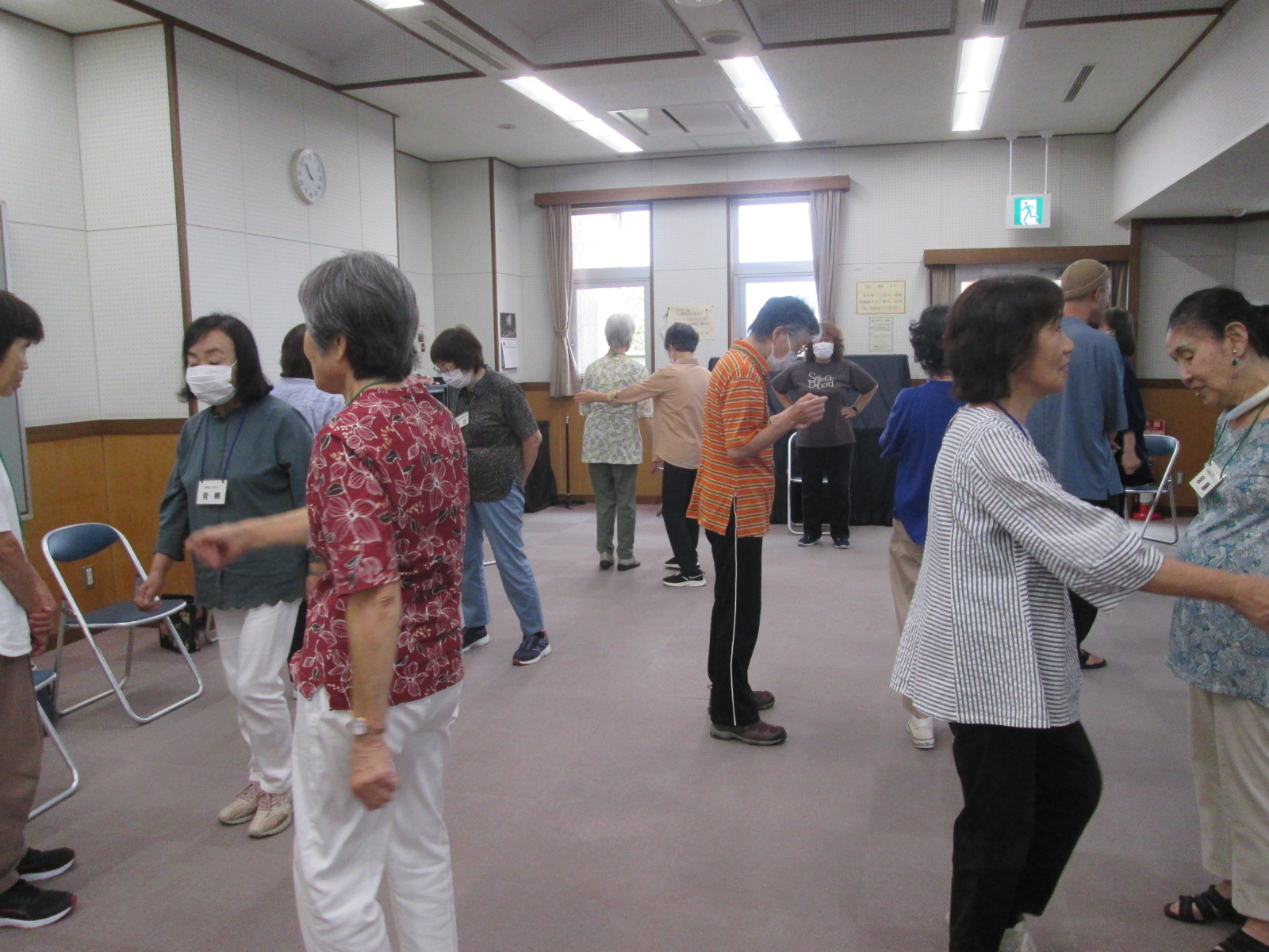 複数人が広い室内でマスクを着用し、音楽や指導に合わせてゲームを行っている様子の写真