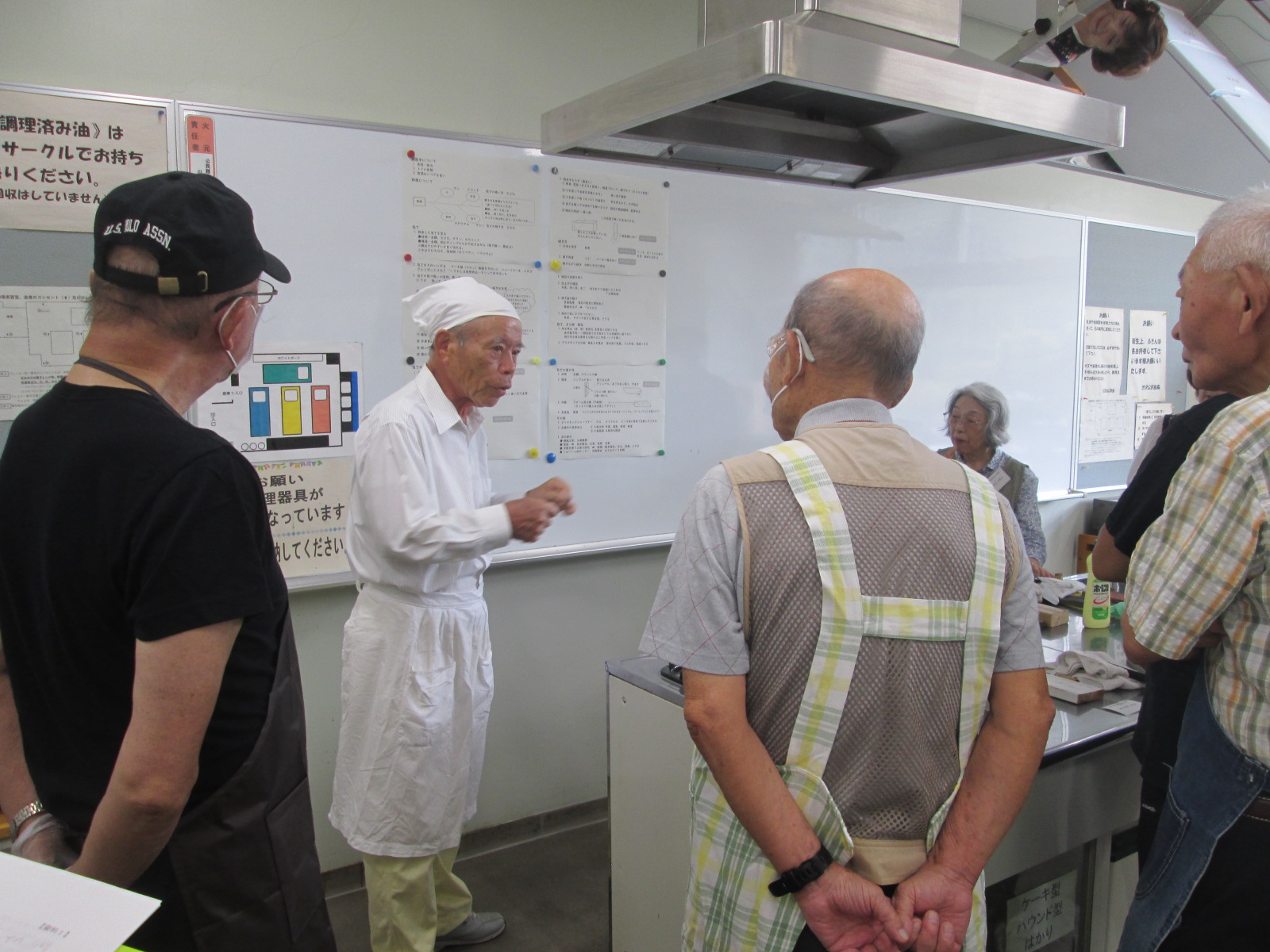 白い調理服を着た講師が複数の参加者に対してホワイトボードを使って説明している写真