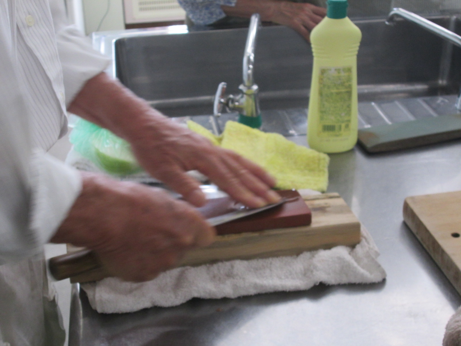 ステンレス製カウンターとシンクの前で、濡らした砥石を使って、手元の包丁の刃を慎重に研いでいる作業のクローズアップ写真